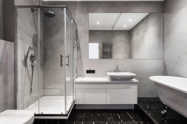 Bathroom with basin, shower cabin, large mirror and chrome silver heater or towel radiator at grey wall. Loft style in new apartment. Modern house with contemporary interior